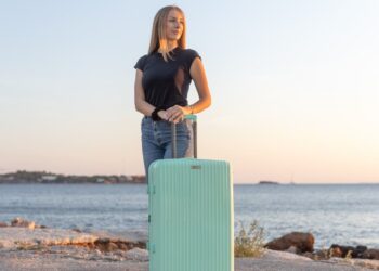 Μεγάλη βαλίτσα τιρκουαζ από πολυπροπυλένιο με ένα μοντέλο ξανθιά να το κρατάει .